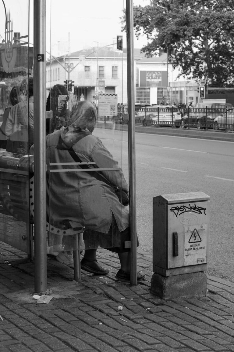 people waiting on a bus stop by the street in black and white