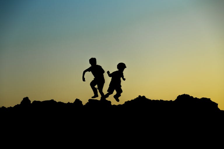 Silhouette of two children joyfully playing outdoors at sunset, capturing a moment of adventure.