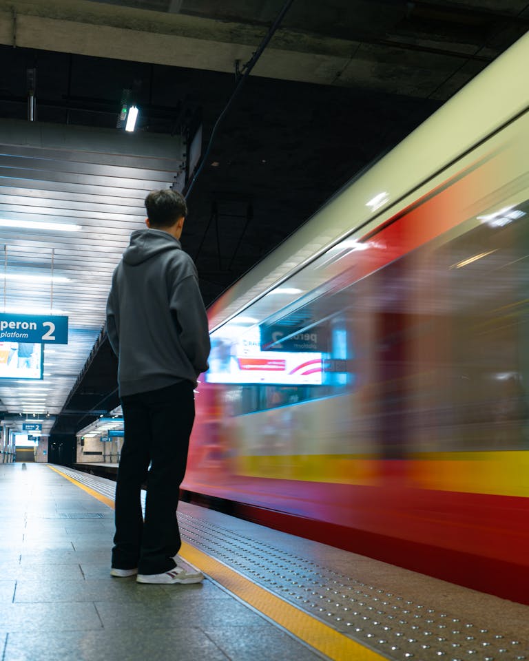 A man stands on a Warsaw subway platform as a train speeds by, capturing urban transit in motion.