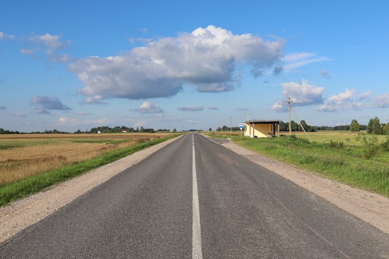 Long stretch of open road in rural Poland, showcasing green fields under a blue sky filled with clouds.