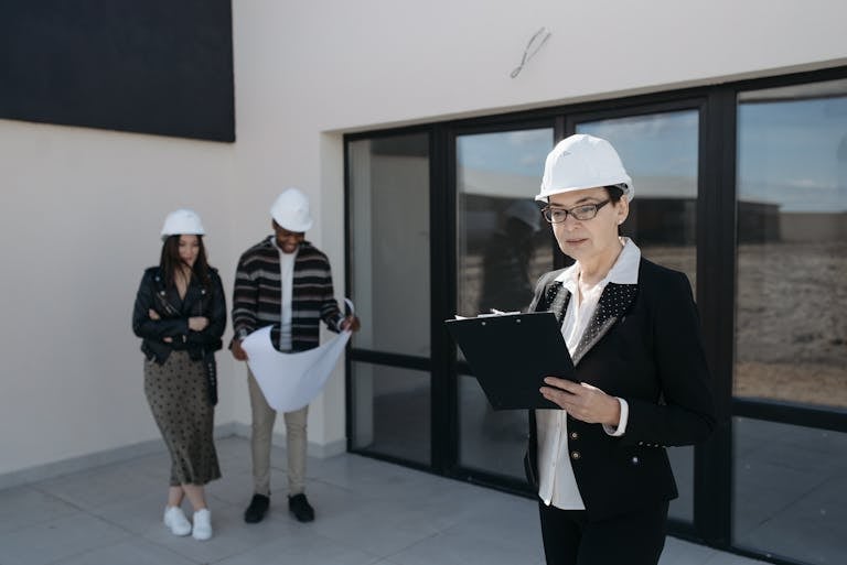 Architects in hard hats examining construction plans at a building site.