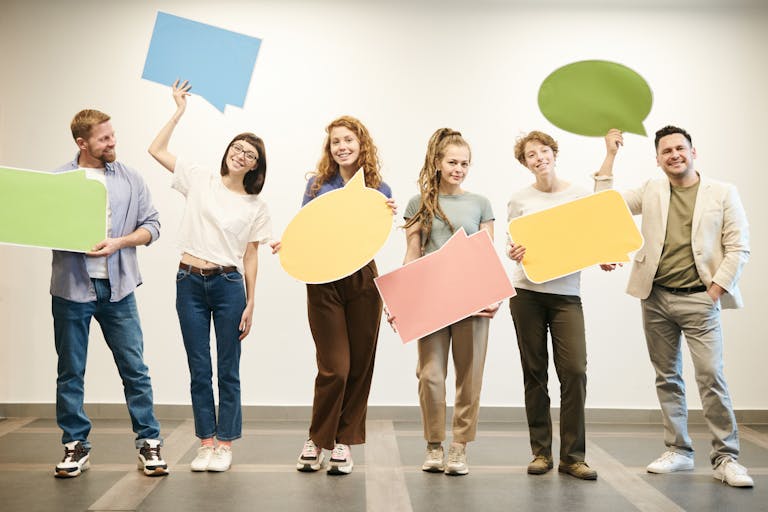 Diverse group of smiling adults holding vibrant speech bubbles indoors.