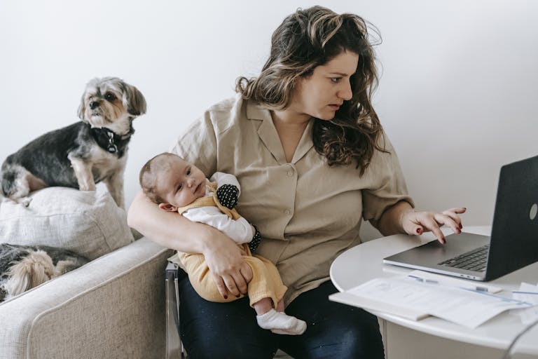 Mother balancing work from home with parenting, holding baby and typing on laptop.