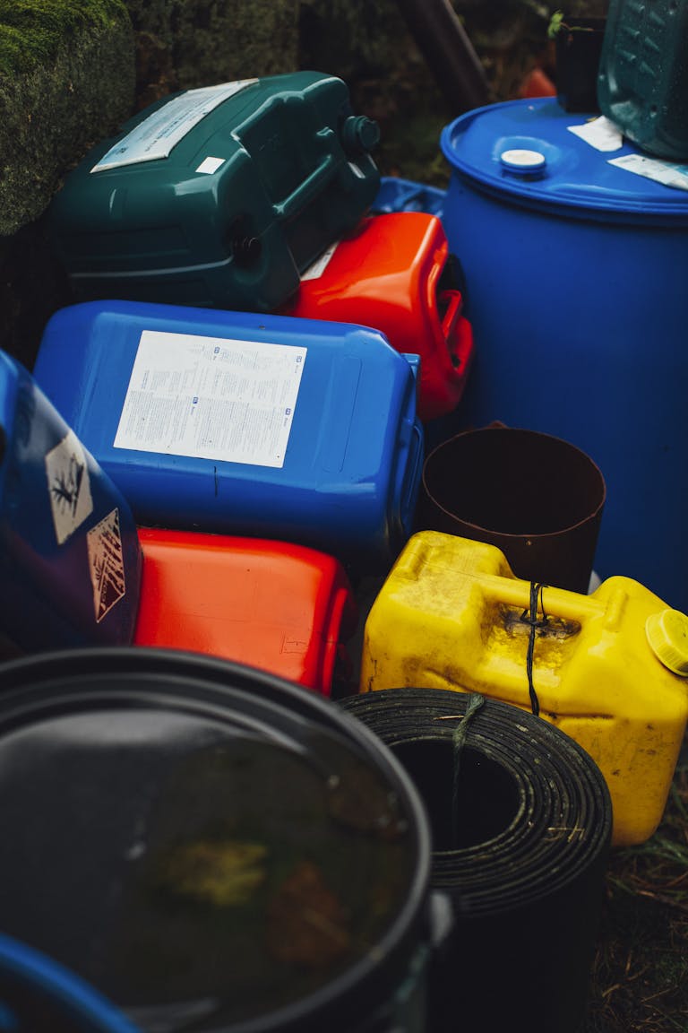 Assorted colorful plastic containers and barrels stacked outdoors, showcasing waste management.