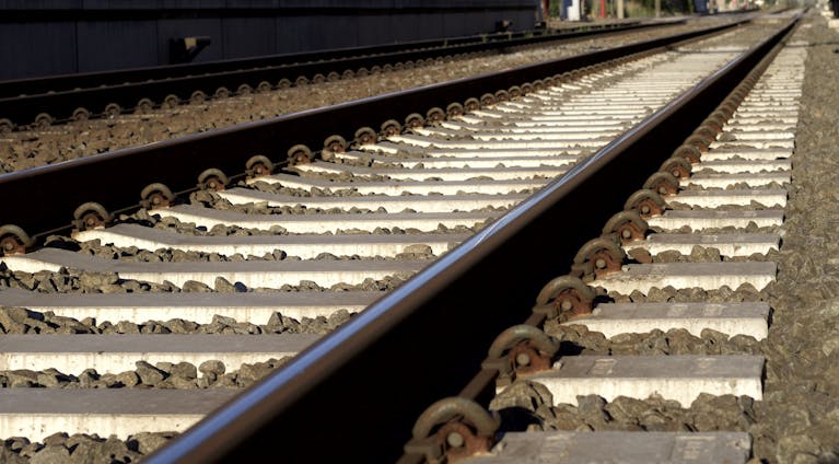 Detailed photo of railway tracks under bright sunlight with stones.