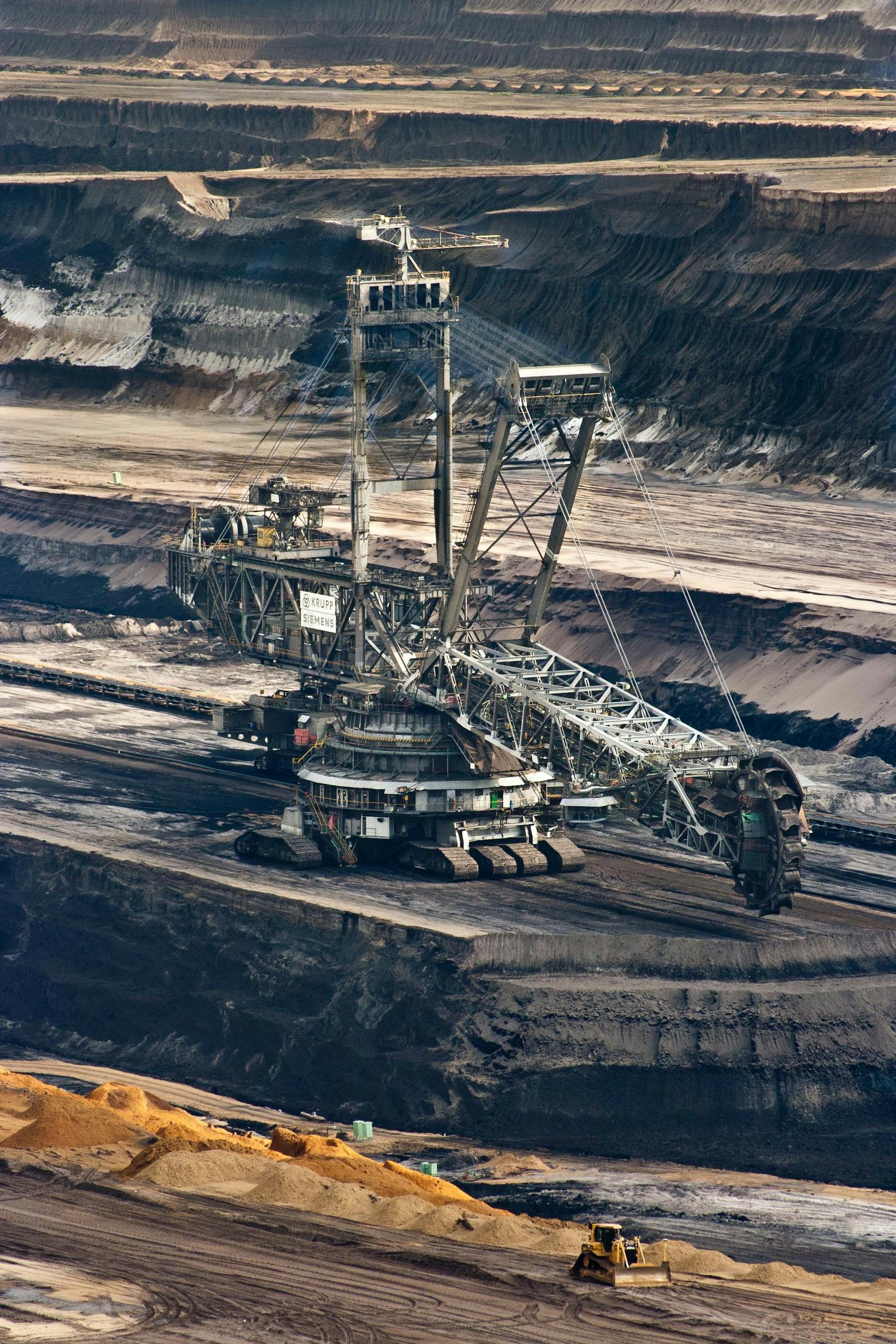 Large bucket wheel excavator operating in an open-pit mine with layered soil and coal.