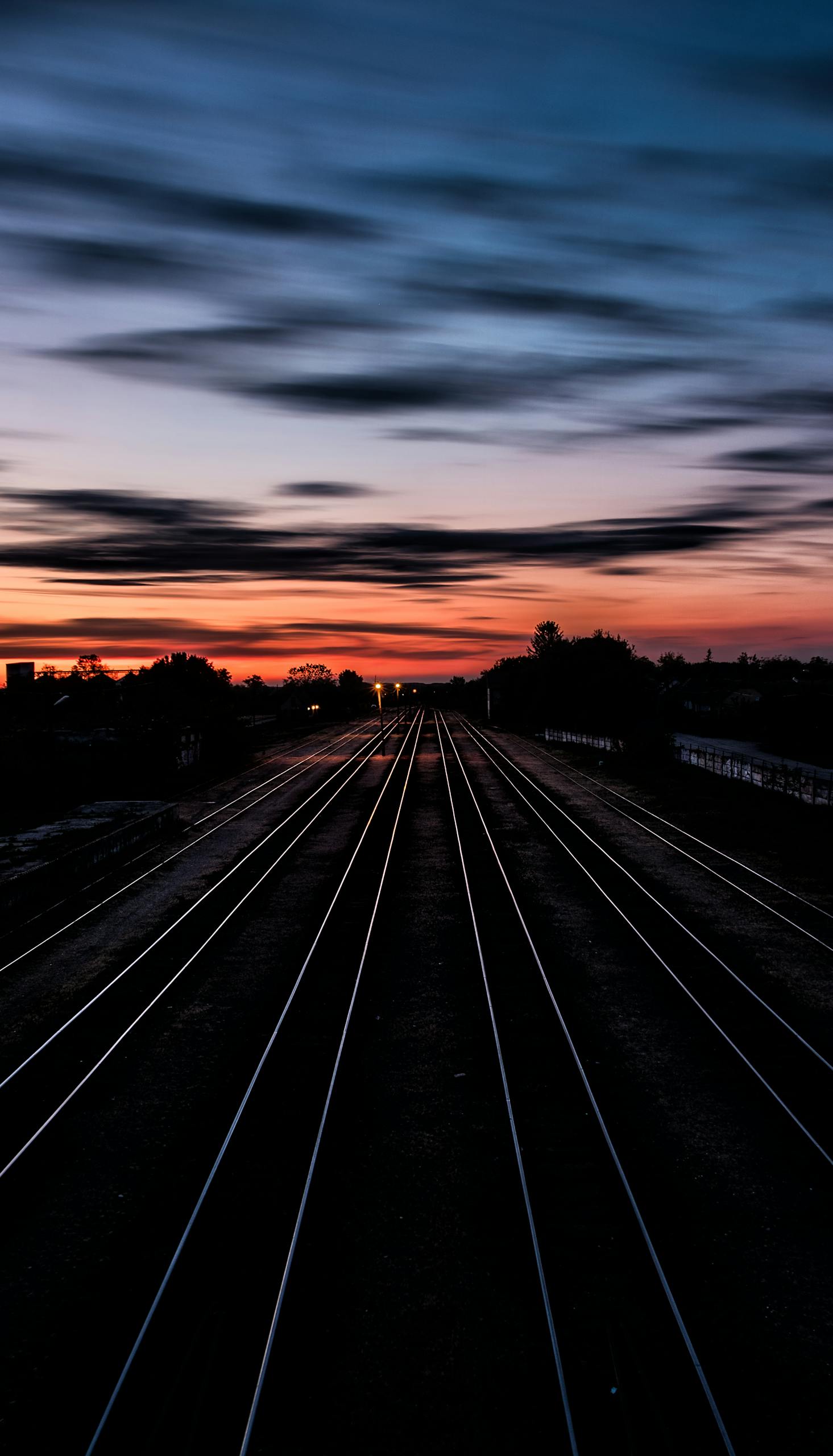 Long railway tracks stretching into the horizon under a dramatic twilight sky.