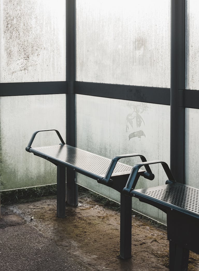 A foggy bus stop with empty benches and steamy, rain-soaked windows.