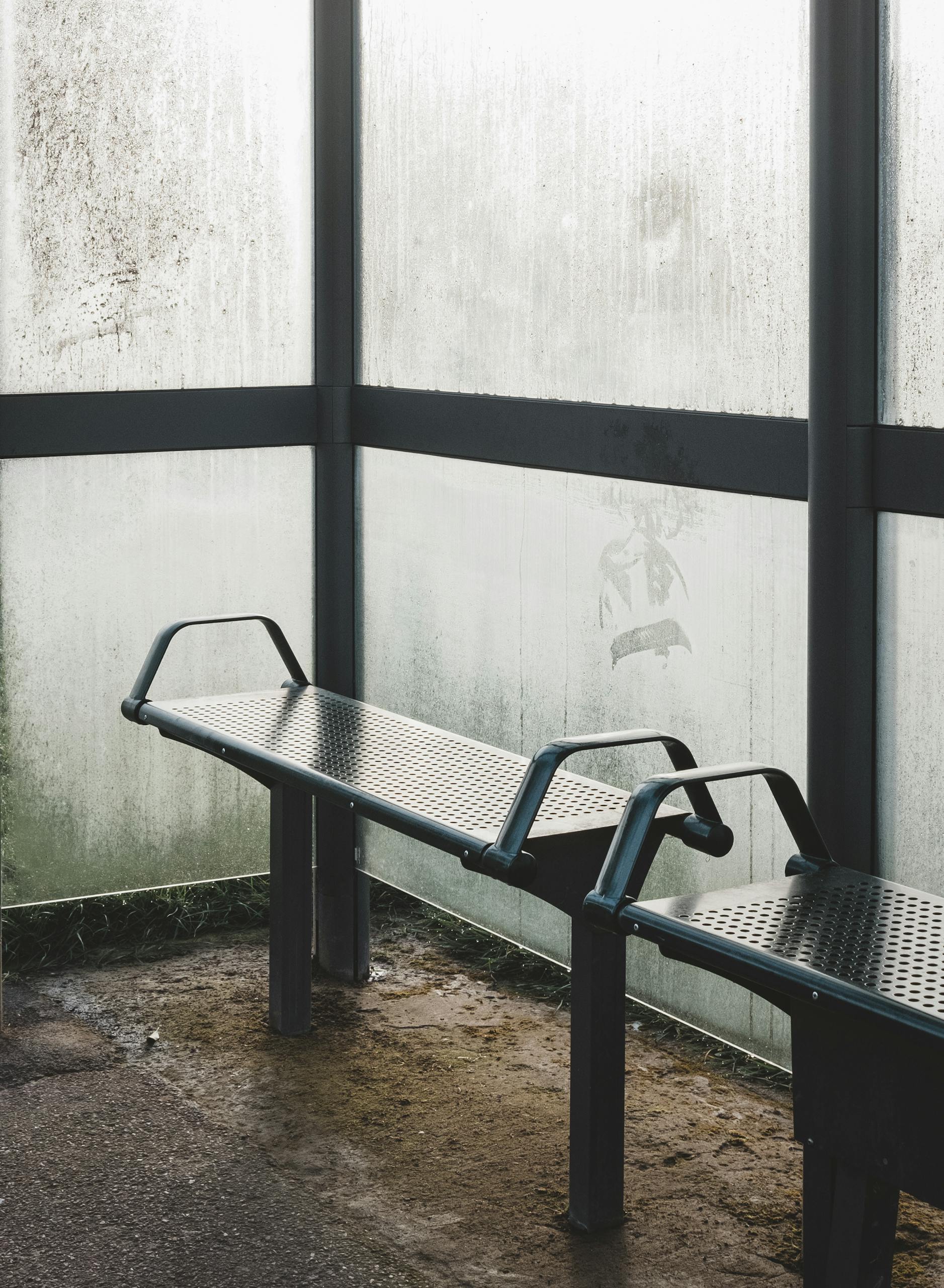 A foggy bus stop with empty benches and steamy, rain-soaked windows.