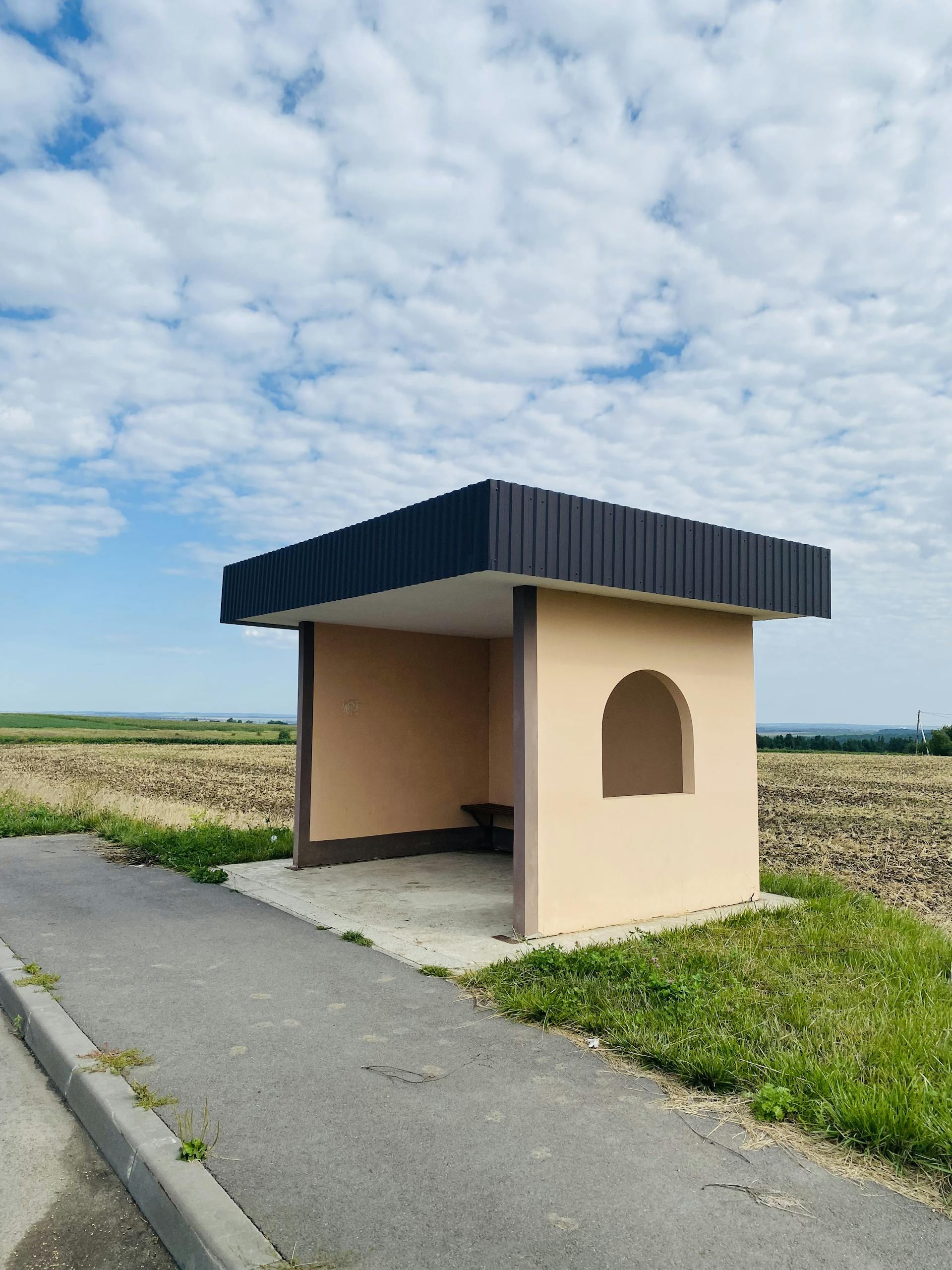 A lonely bus stop structure in a rural landscape under a cloudy sky.