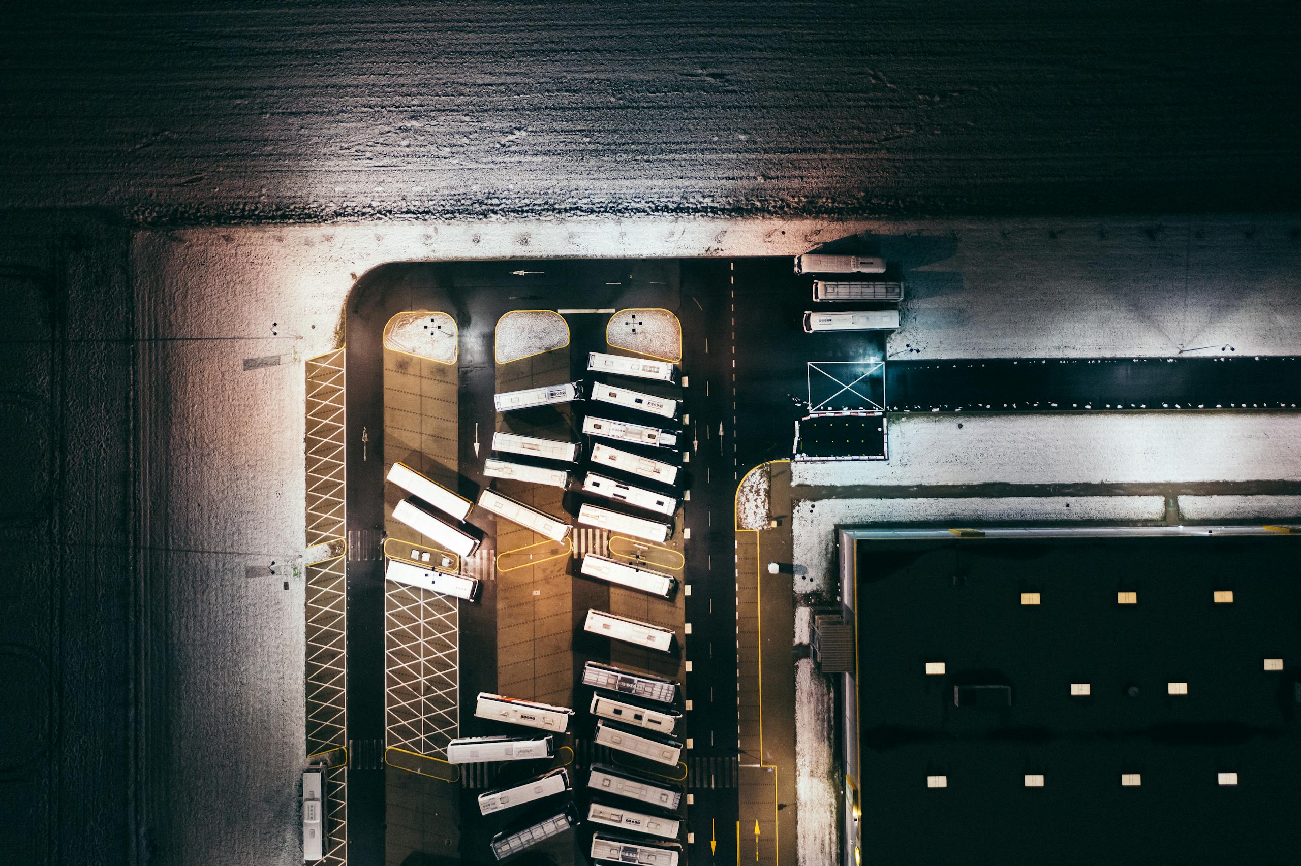 Aerial perspective of buses parked in a snow-covered depot at night, illuminated by artificial lights.