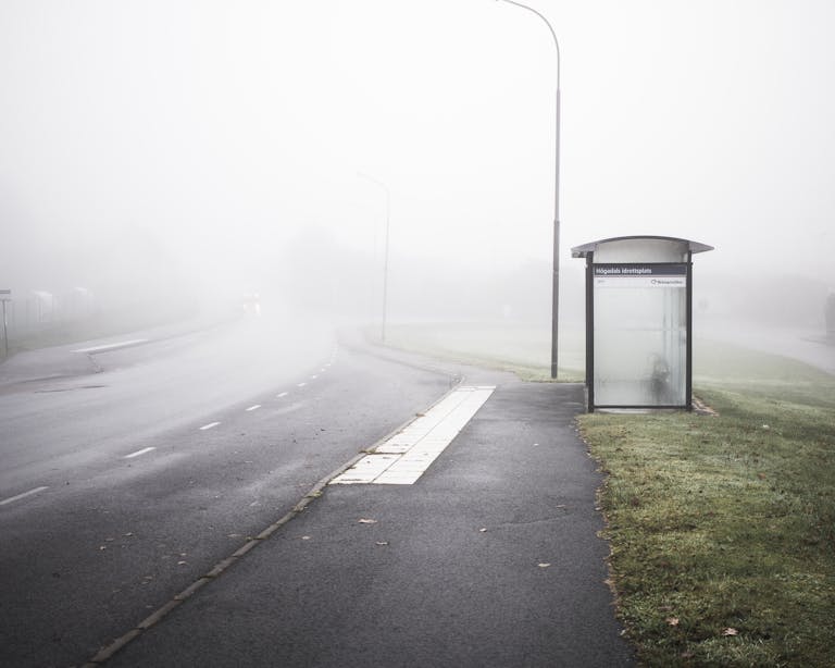 Eerie foggy morning scene at a lonely bus stop on an empty road in Karlshamn, Sweden.