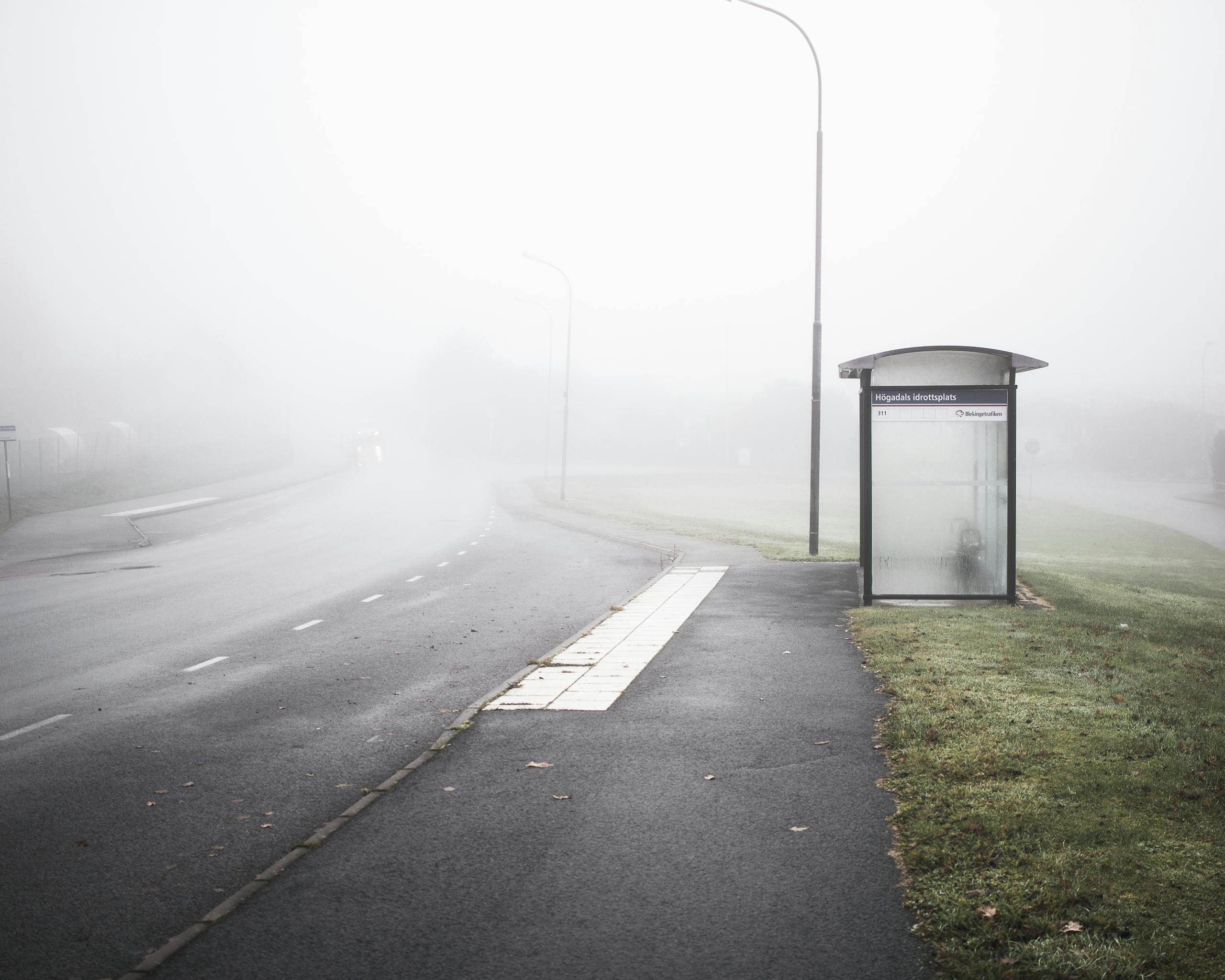 Eerie foggy morning scene at a lonely bus stop on an empty road in Karlshamn, Sweden.