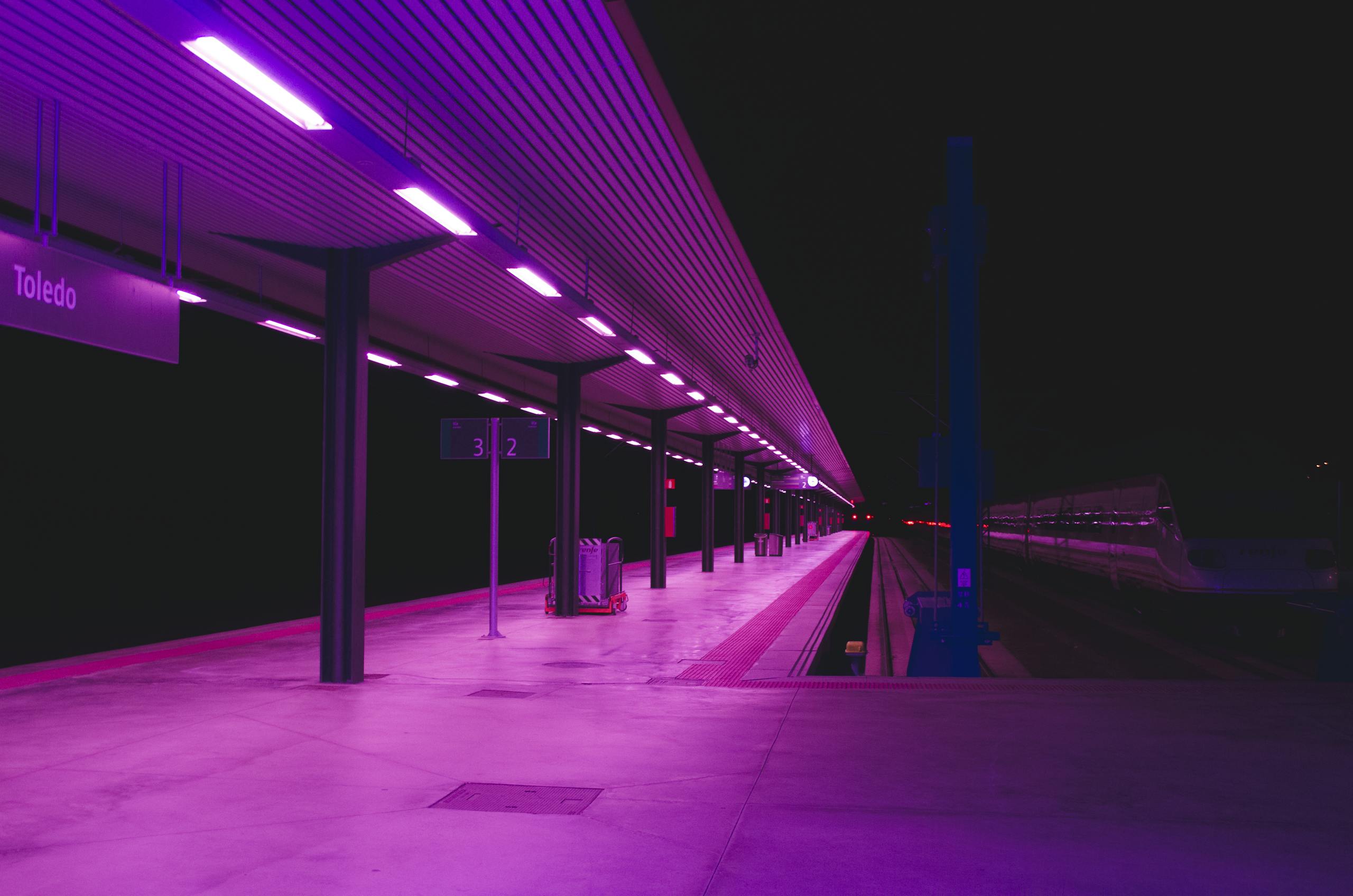 Explore the vibrant neon-lit train station platform in Toledo at night, showcasing urban architecture.