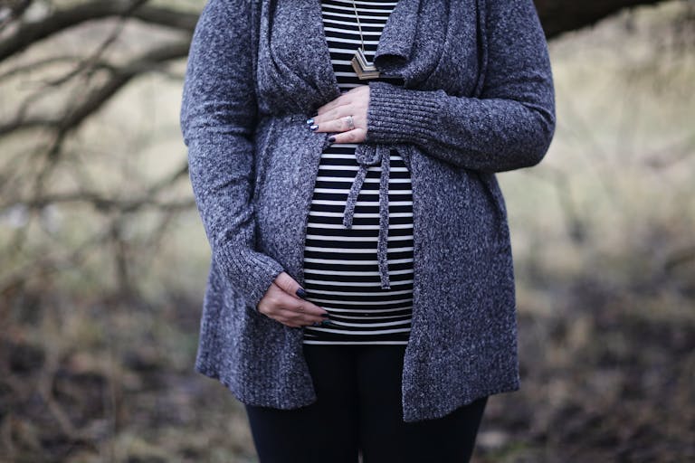 Pregnant woman in striped shirt and cozy sweater outdoors, embracing motherhood.