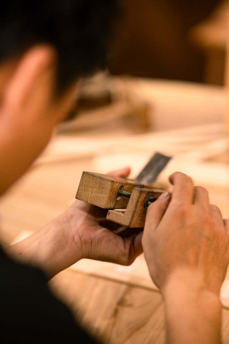 A craftsman focuses on adjusting a wooden tool, showcasing fine woodworking skills in a workshop.