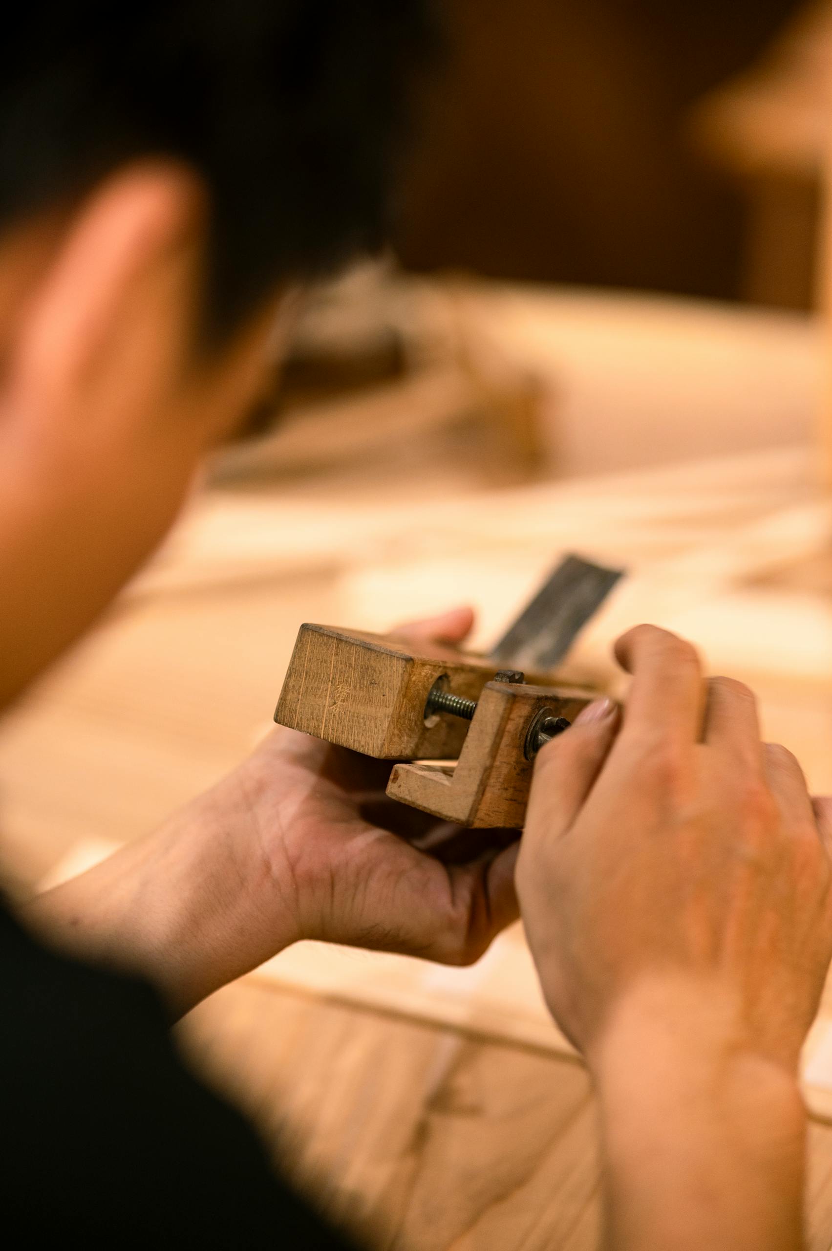 A craftsman focuses on adjusting a wooden tool, showcasing fine woodworking skills in a workshop.