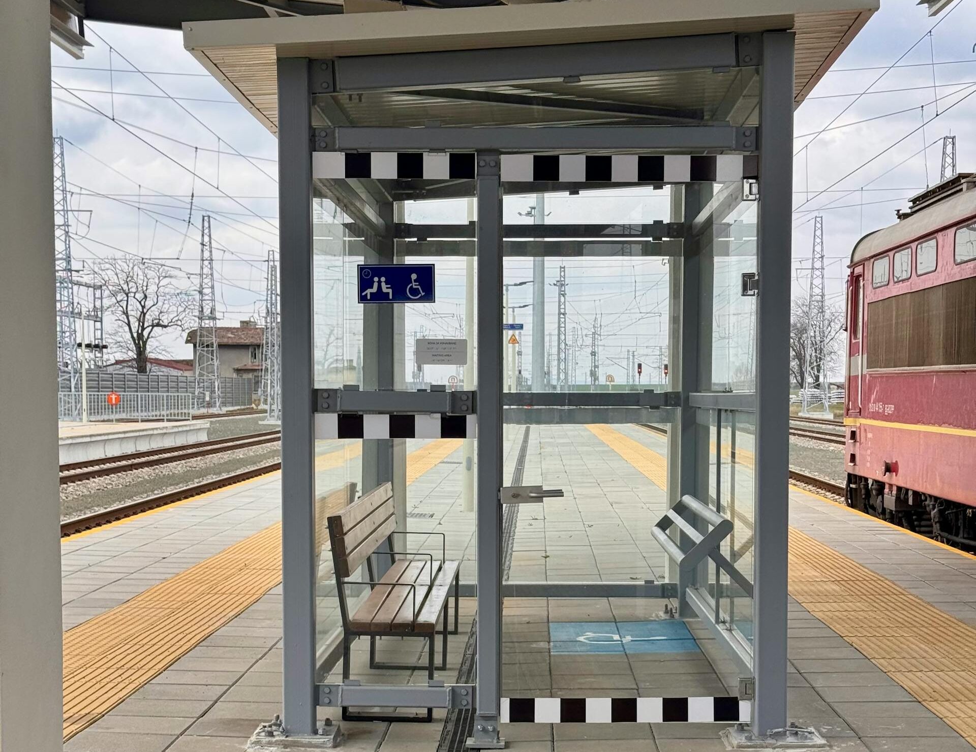 A modern accessible waiting area at a train station platform, featuring clear signage.