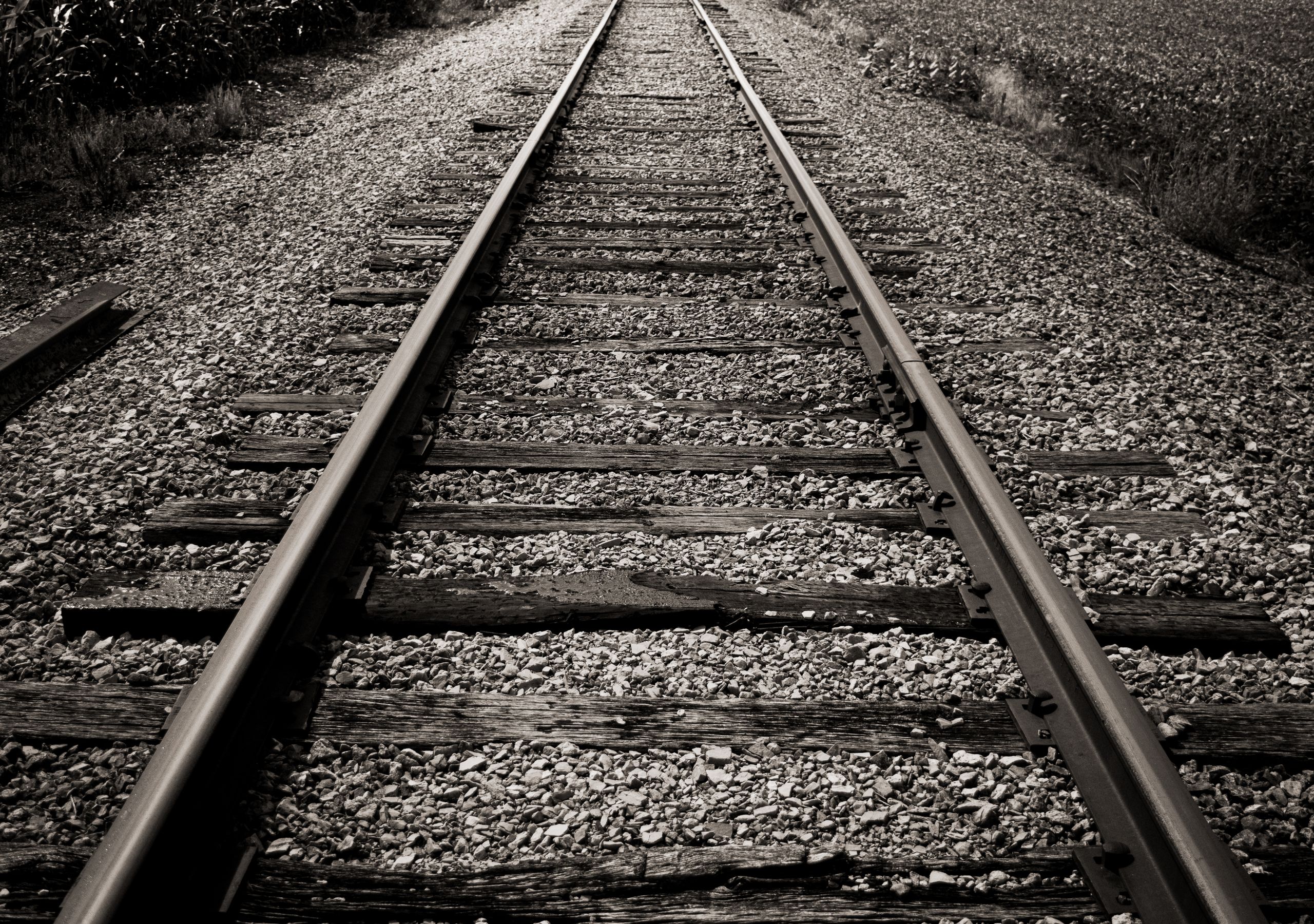 Black and white photo of rustic railroad tracks disappearing into the distance.