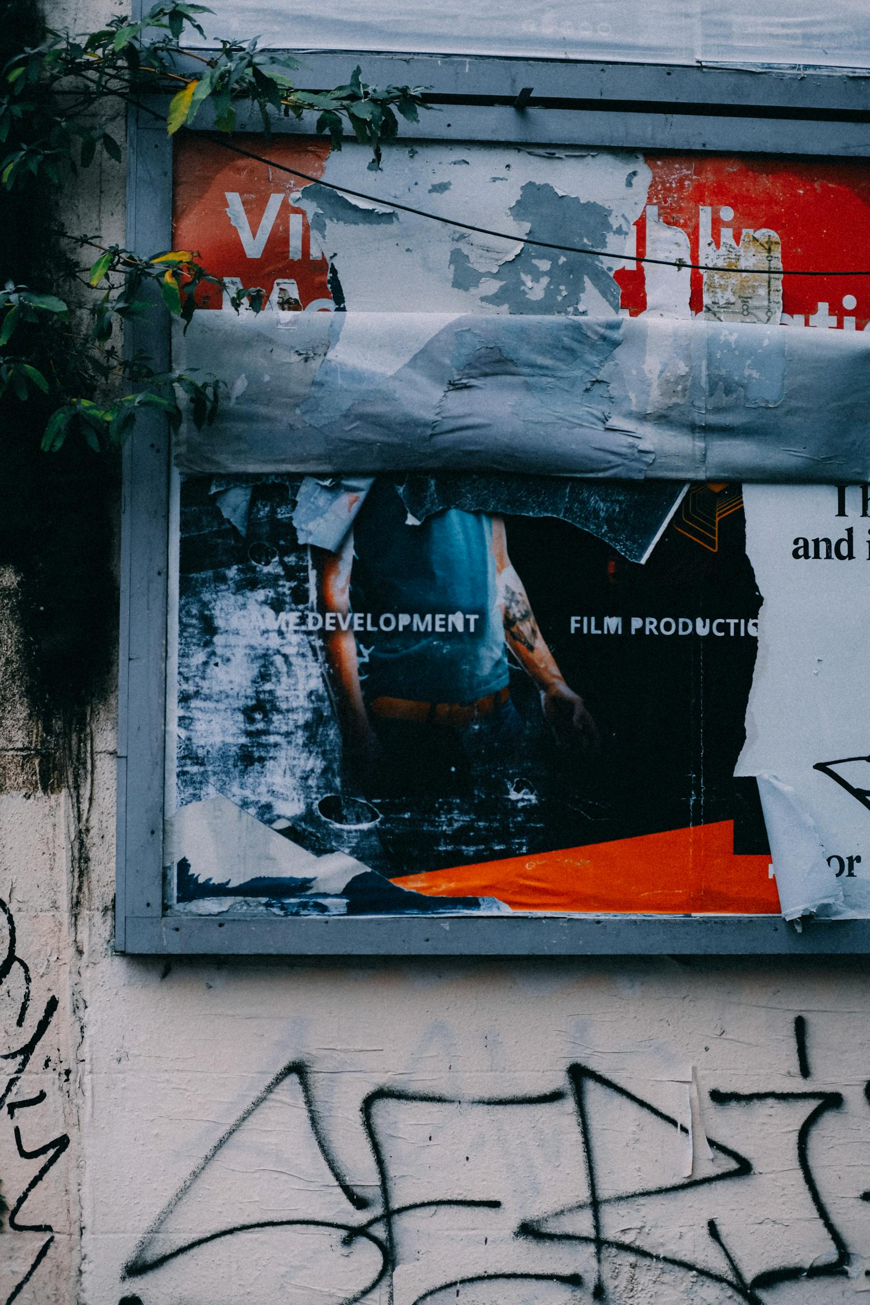 Vandalized urban billboard with graffiti and peeling posters.