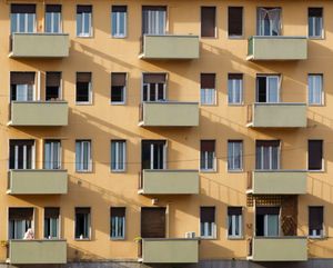 Facade of an apartment building with multiple balconies and windows in sunlight.