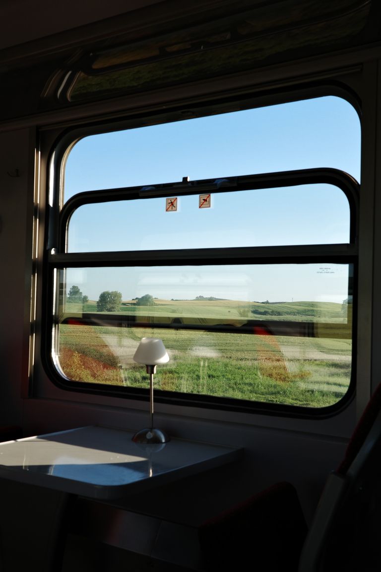 Train window view of Polish countryside with fields and hills under a clear blue sky.